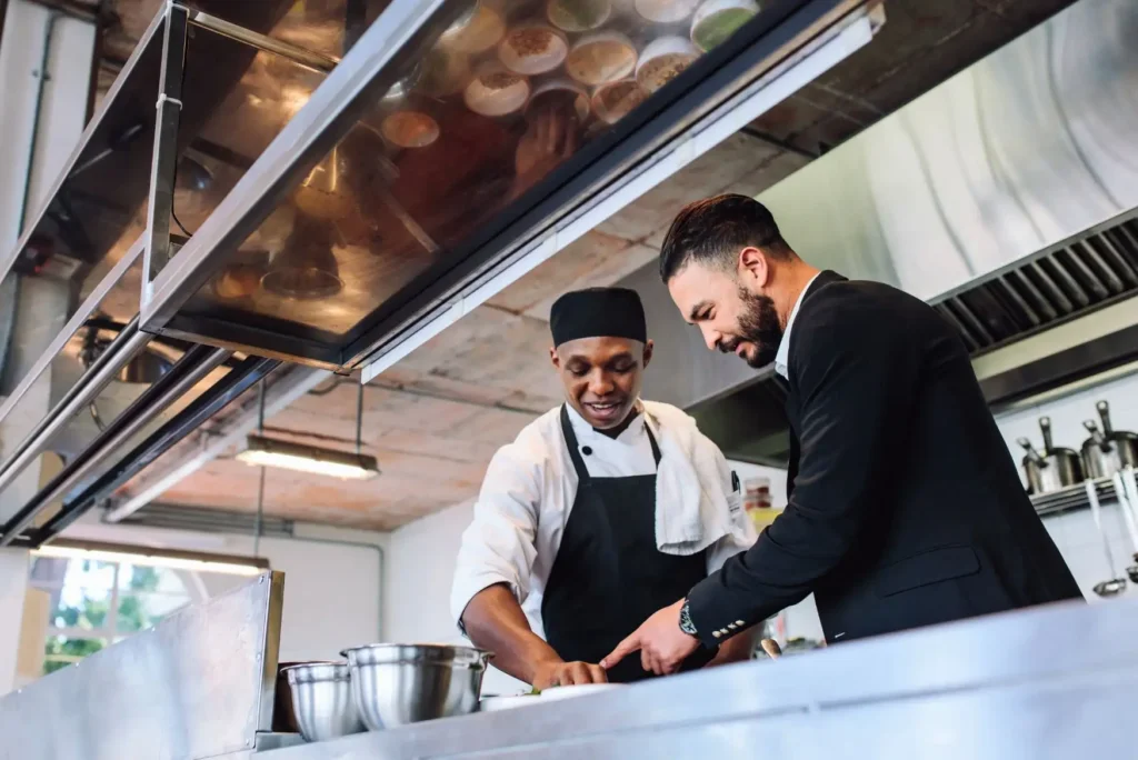 Consultor de Bajo el Mantel impartiendo capacitación para restaurantes a un cocinero sobre estandarización de platillos y flujos de trabajo en cocina.